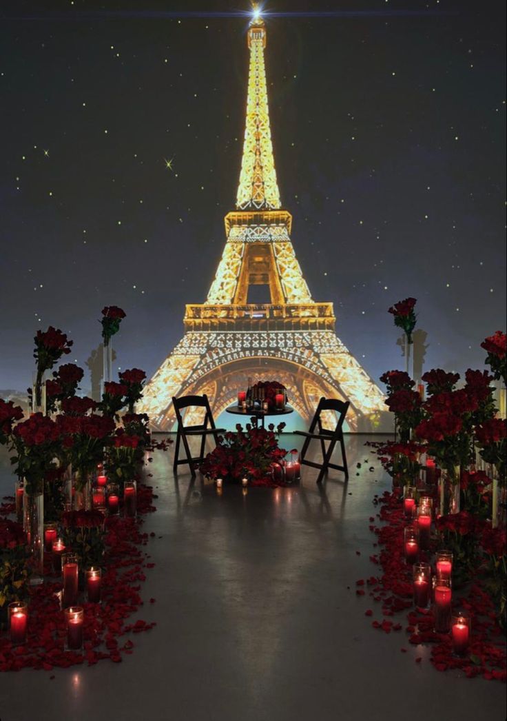 the eiffel tower lit up at night with red roses around it and candles on the ground