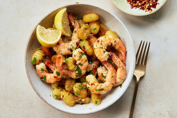 a white bowl filled with shrimp and potatoes next to a plate of lemon wedges