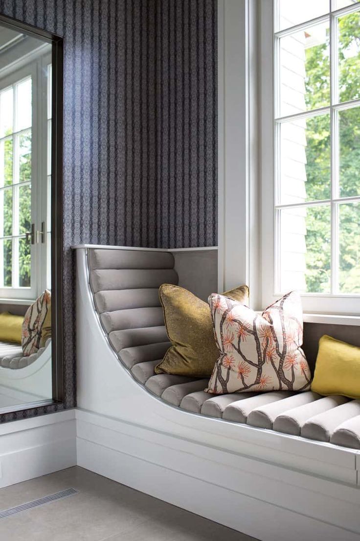 a window seat with pillows on it and a mirror in the corner next to it