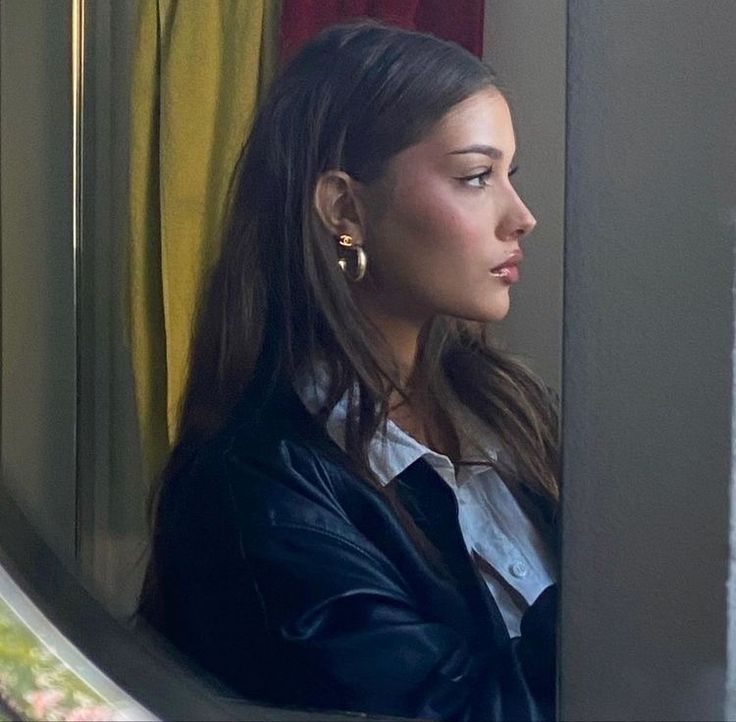 a woman is looking out the window while wearing earrings and a black leather jacket