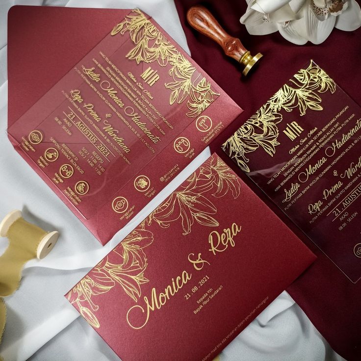 two red and gold wedding cards sitting on top of a table