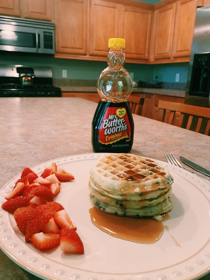 a white plate topped with waffles covered in syrup next to sliced strawberries