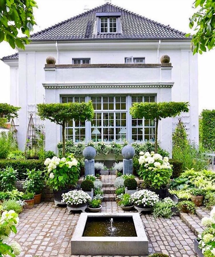 a white house with lots of potted plants and water fountain in the front yard