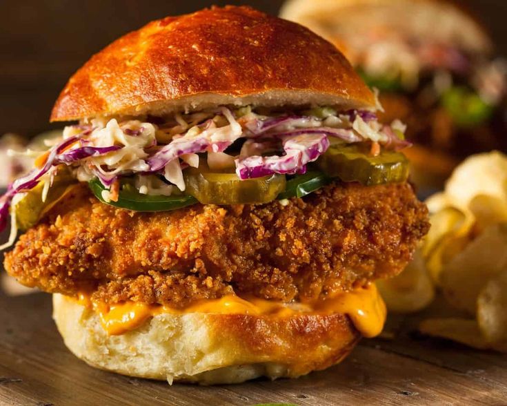 a fried chicken sandwich with coleslaw and pickles on a wooden cutting board