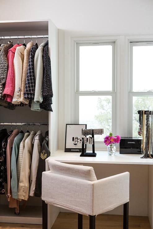 a white chair sitting in front of a window next to a shelf with clothes on it