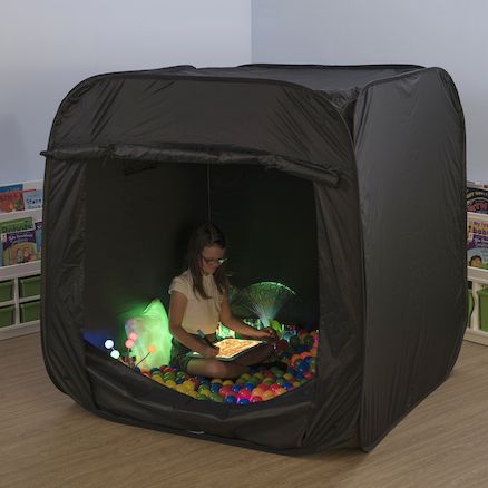 a woman is sitting in a black tent with lights on the floor and playing inside