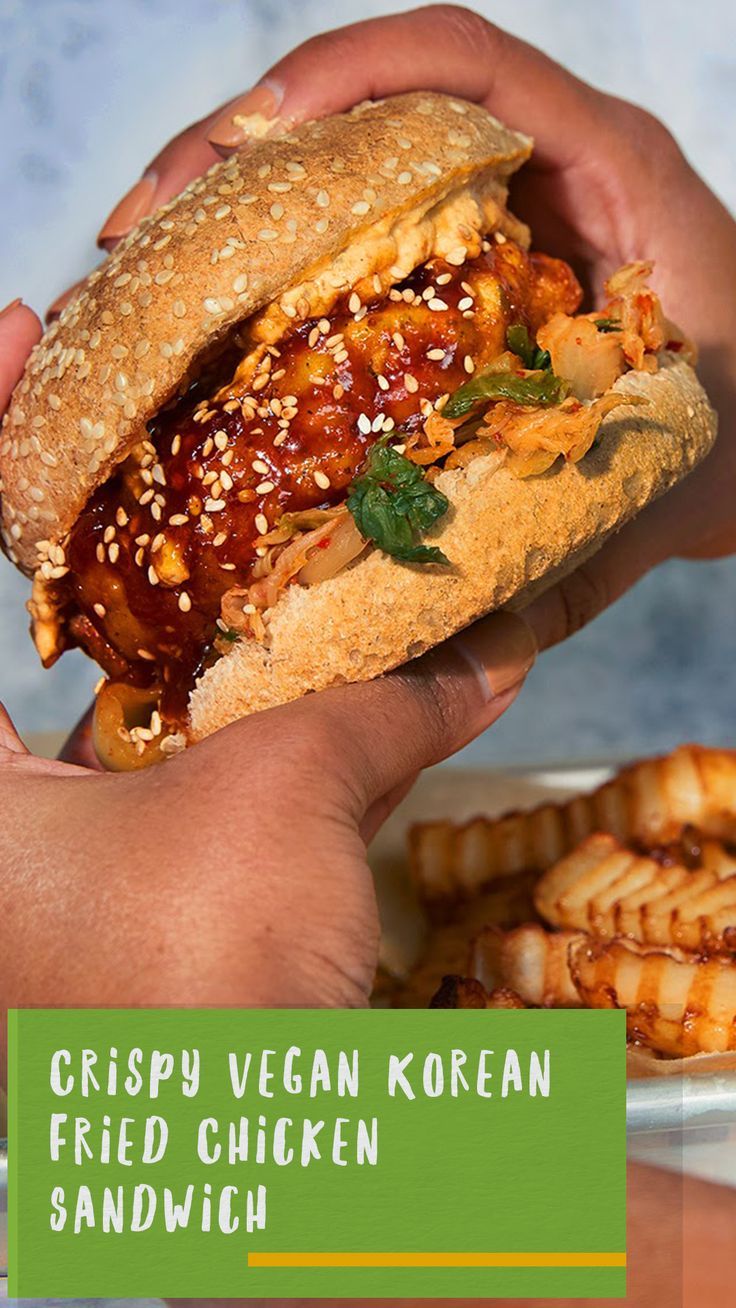 a person holding a sandwich in their hand with the caption crispy vegan korean fried chicken sandwich