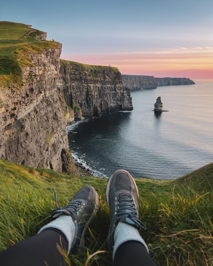 someone's feet resting on the edge of a cliff overlooking the ocean at sunset