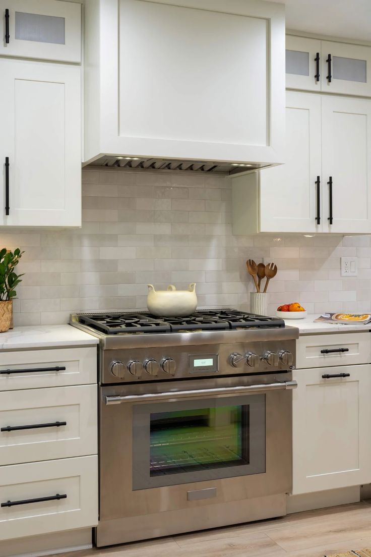 a stove top oven sitting inside of a kitchen next to white cupboards and drawers