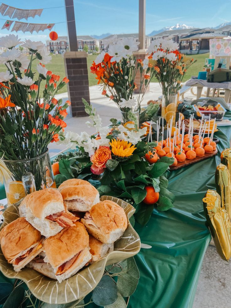 sandwiches and orange flowers on a green table cloth at an outdoor party with candles, candy sticks, and flower centerpieces