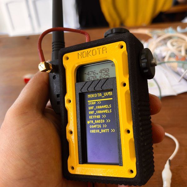 a hand holding a yellow and black device on top of a wooden table with wires