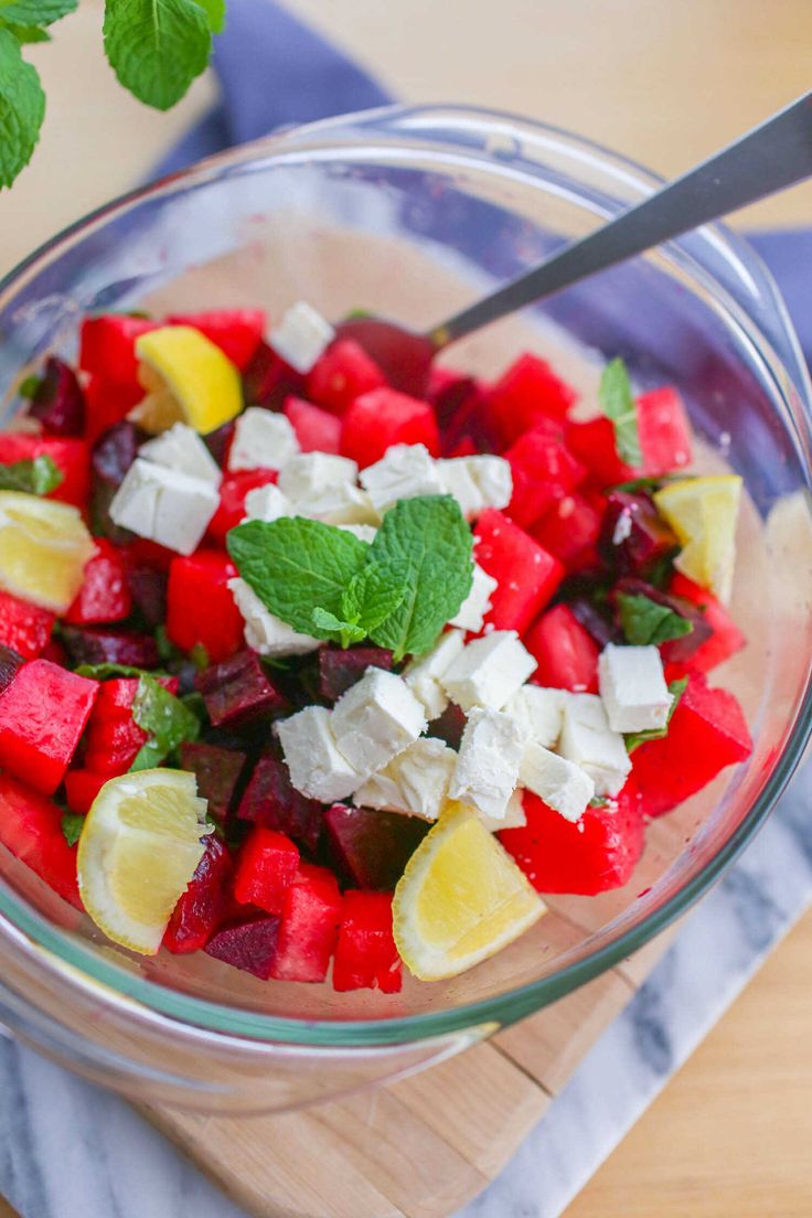 a glass bowl filled with watermelon, feta cheese and lemon wedges