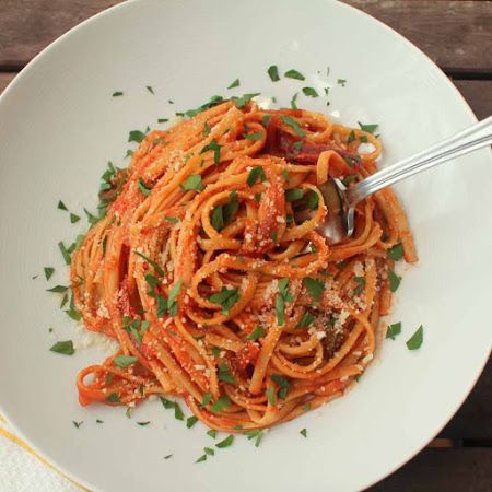 a white bowl filled with pasta and topped with parmesan cheese, garnished with fresh herbs