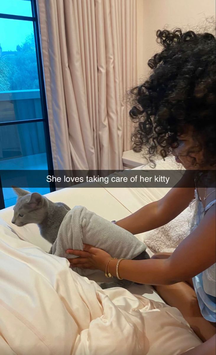 a woman laying in bed next to a cat on top of a white sheet with the caption she loves taking care of her kitty