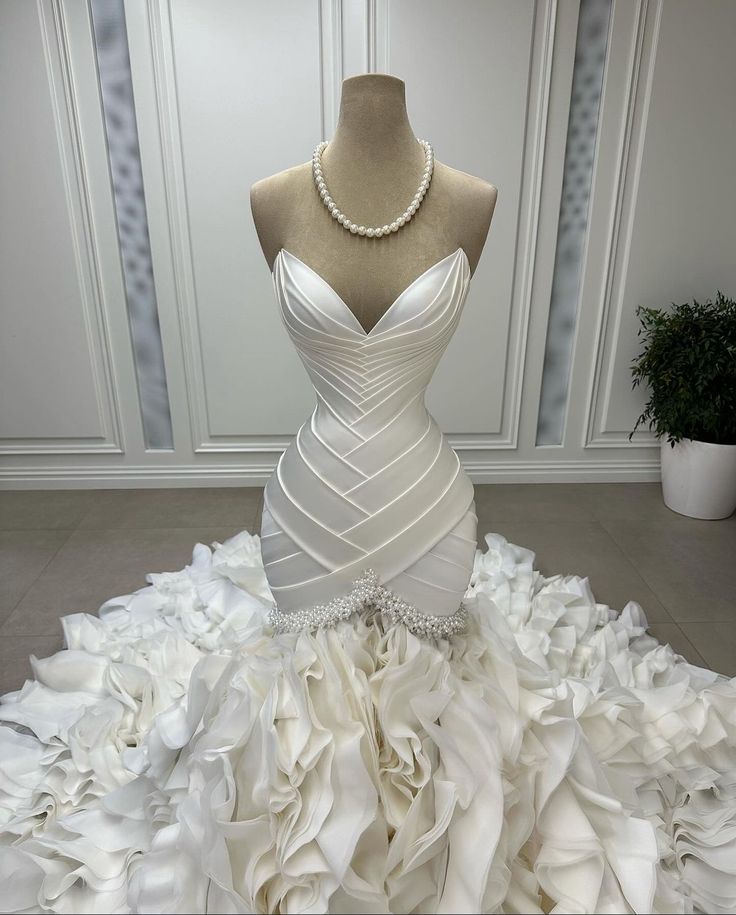 a white wedding dress on display in front of a mannequin wearing a pearl necklace