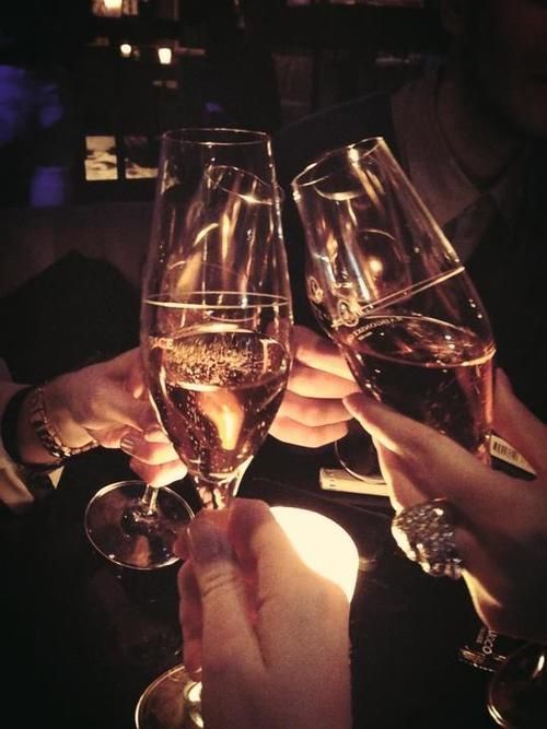 three people holding up wine glasses in front of each other with their hands on the table