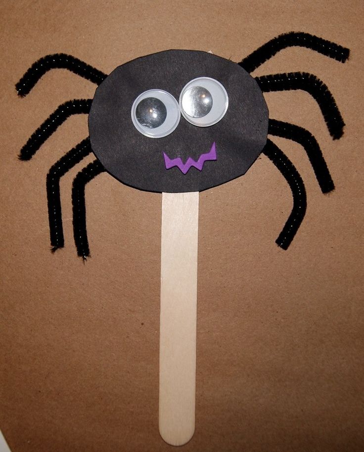 a paper plate with a spider on it and eyes painted on the side, sitting on top of a wooden stick