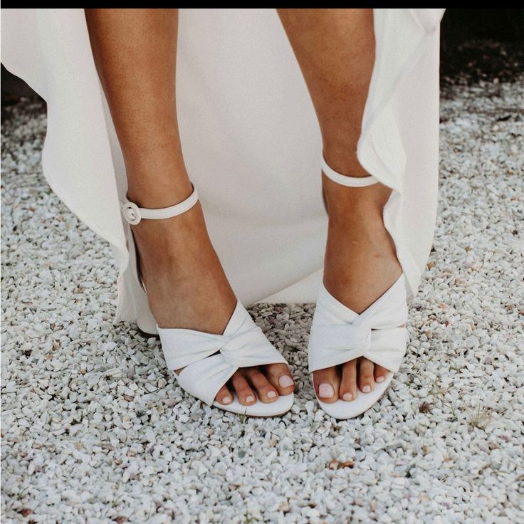 a close up of a person's feet wearing white sandals and a long dress