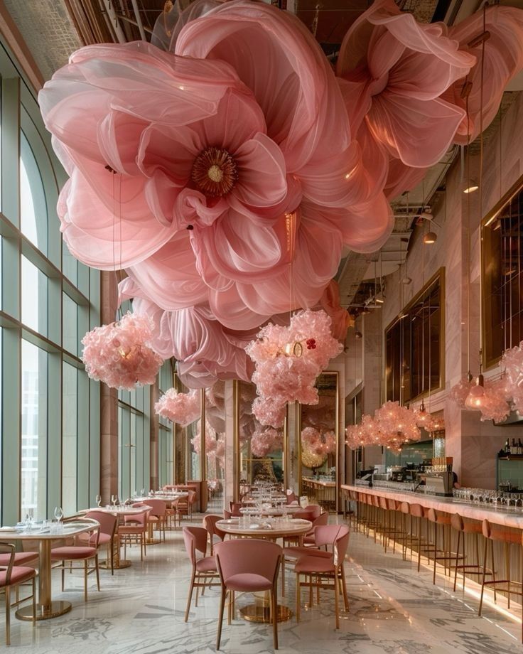 the interior of a restaurant with large pink flowers hanging from the ceiling and tables set up