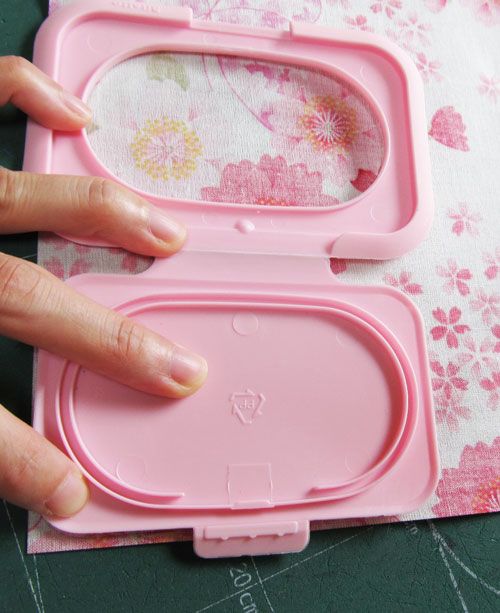 a hand is touching the lid of a pink plastic case with flowers on it,