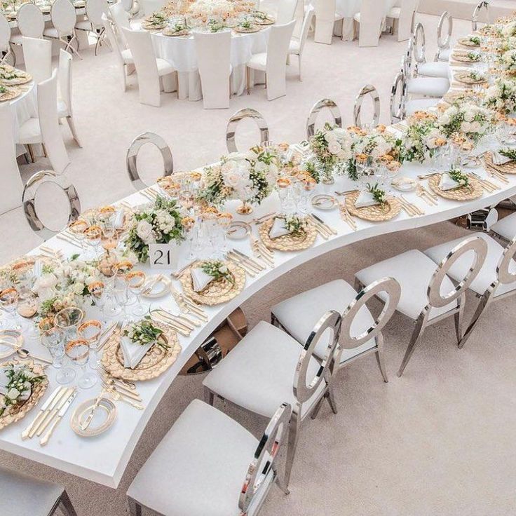 a long table is set up with white chairs and flowers on it for a formal function