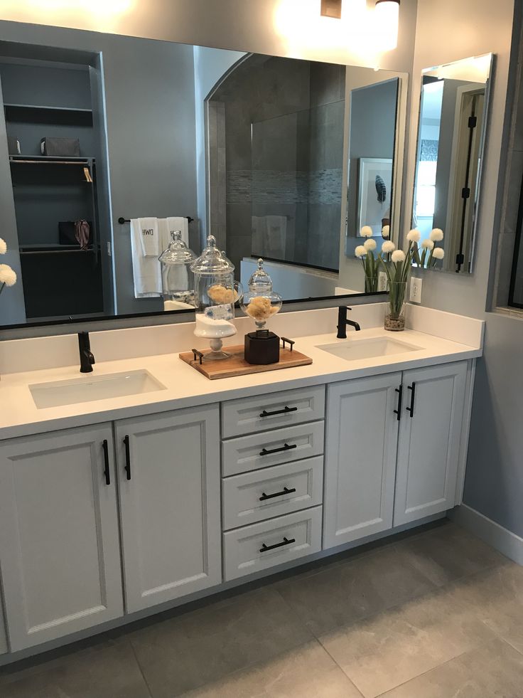 a bathroom with double sinks and large mirror above it's countertop, along with two vases filled with flowers