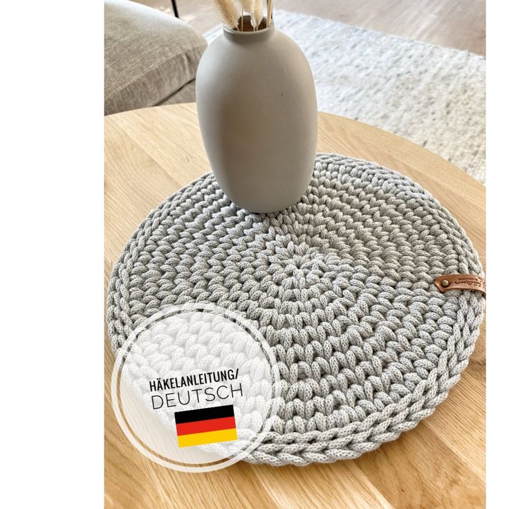 a white vase sitting on top of a wooden table next to a gray round rug