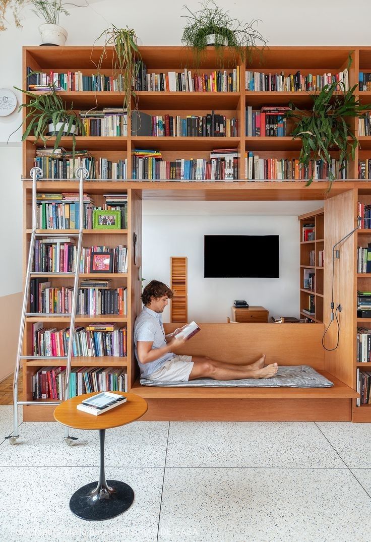 a person sitting on a bed in front of a bookshelf with shelves full of books