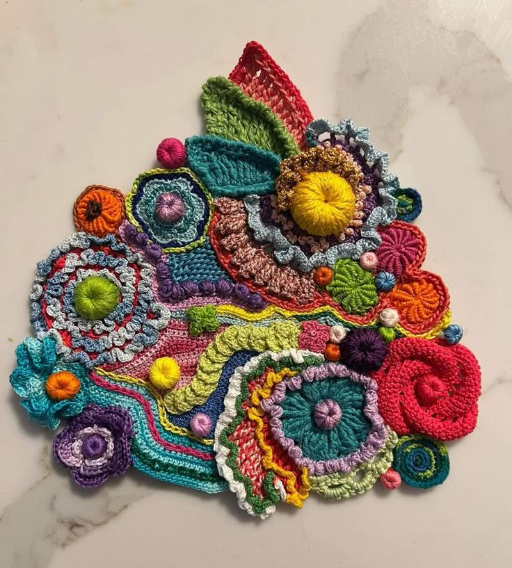 crocheted flowers and leaves on a white surface with marble top, closeup