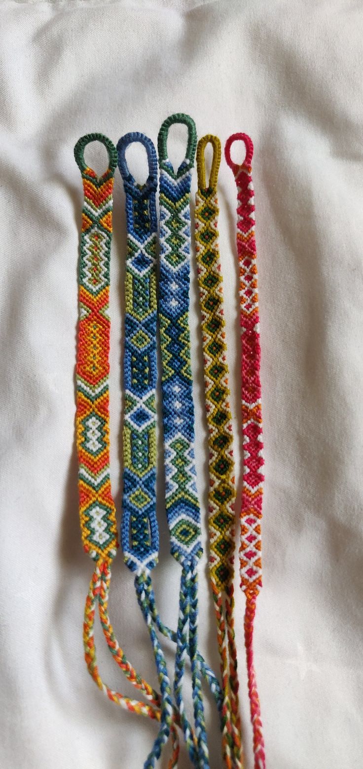 four different colored bracelets are on a white sheet and one is tied to a string