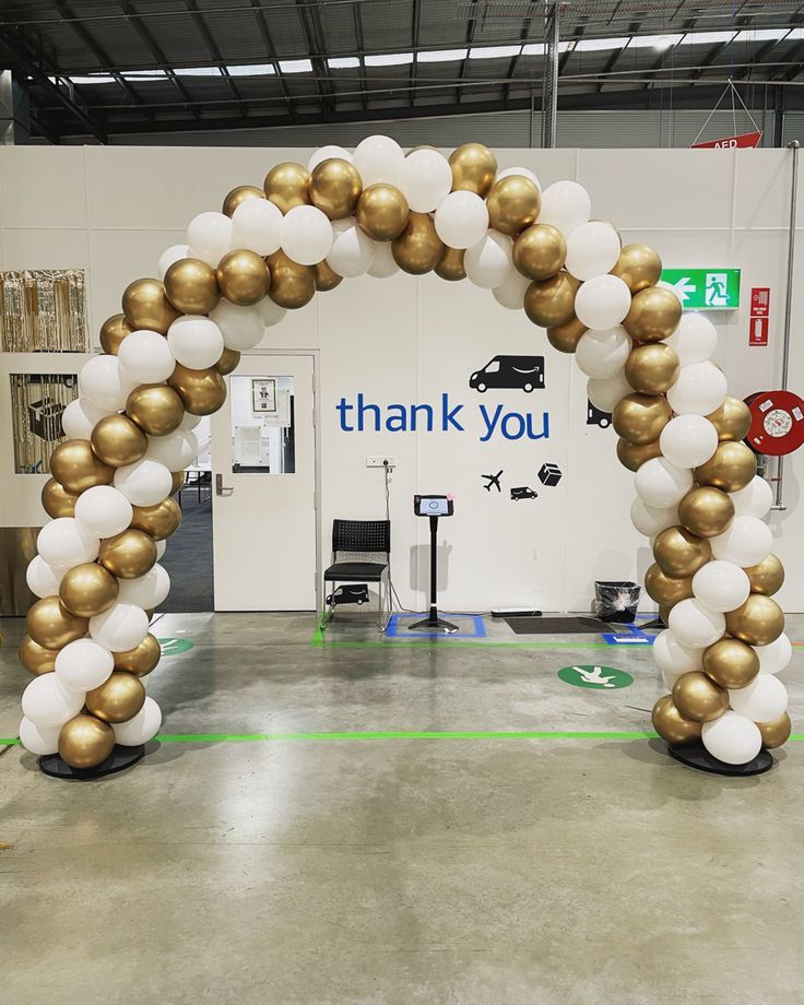 an arch made out of gold and white balloons with thank you written on the side