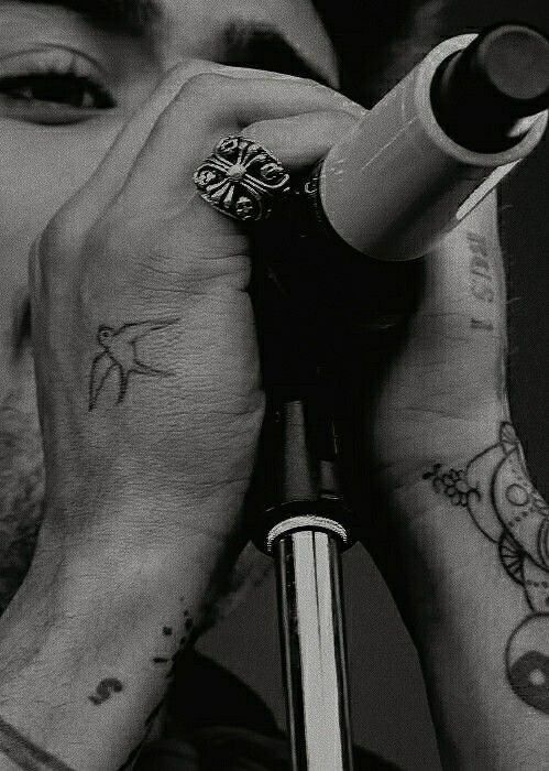 a close up of a person holding a pen to their face with tattoos on his hands