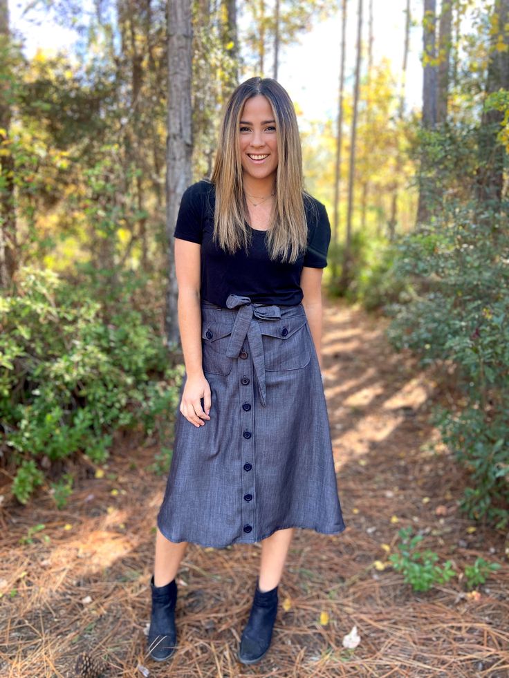 a woman standing in the middle of a forest wearing a blue skirt and black shirt