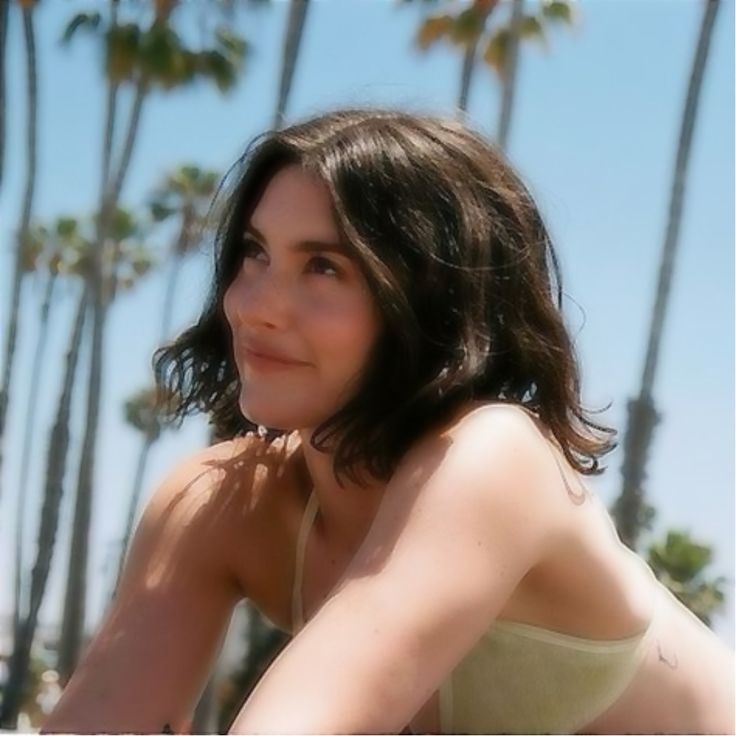 a woman sitting on the beach with palm trees in the backgroung and looking at the camera