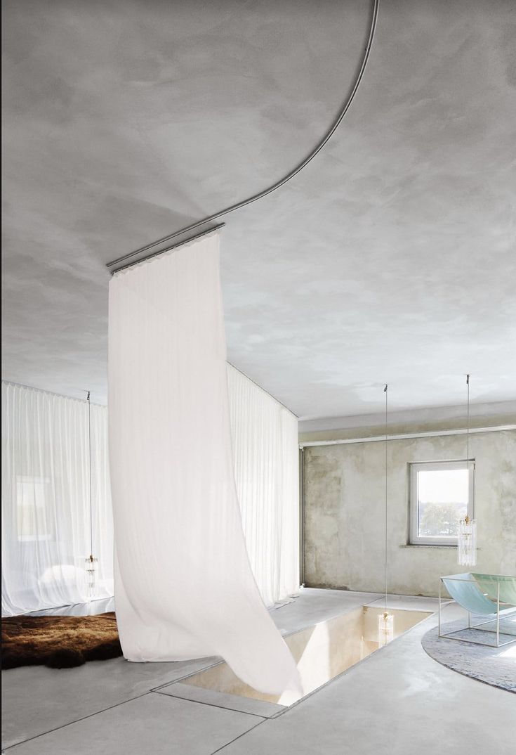 an empty room with white drapes hanging from the ceiling and a bed in the corner