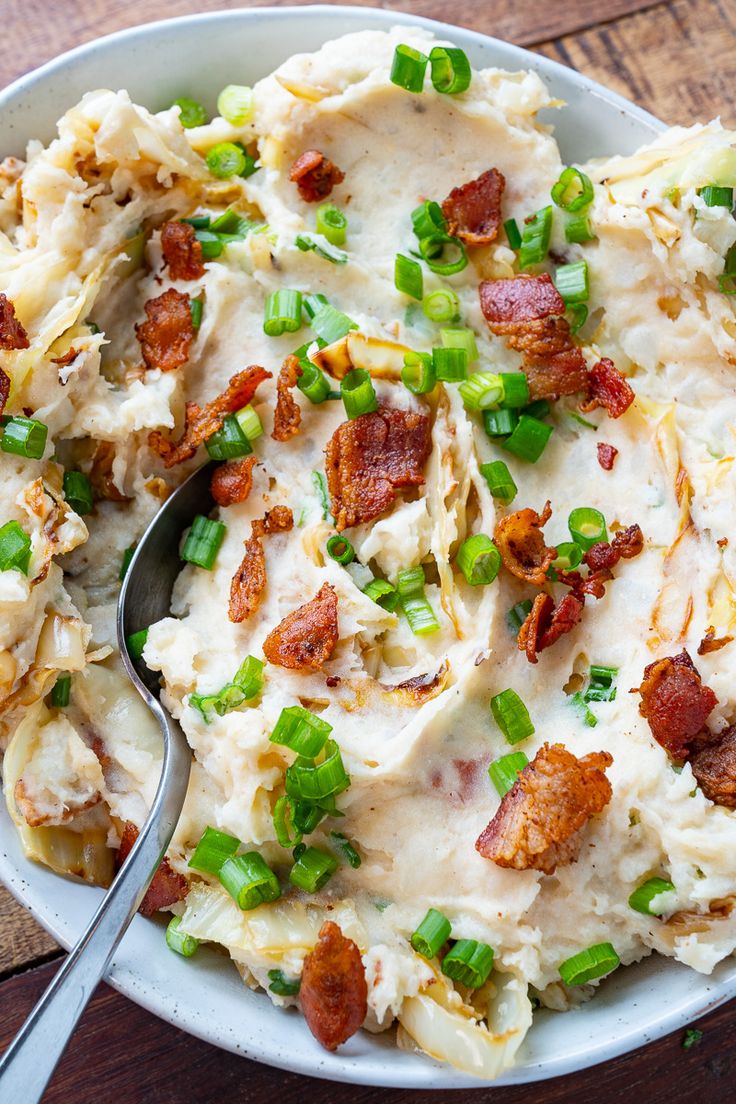 a bowl filled with mashed potatoes covered in bacon and green onions next to a spoon