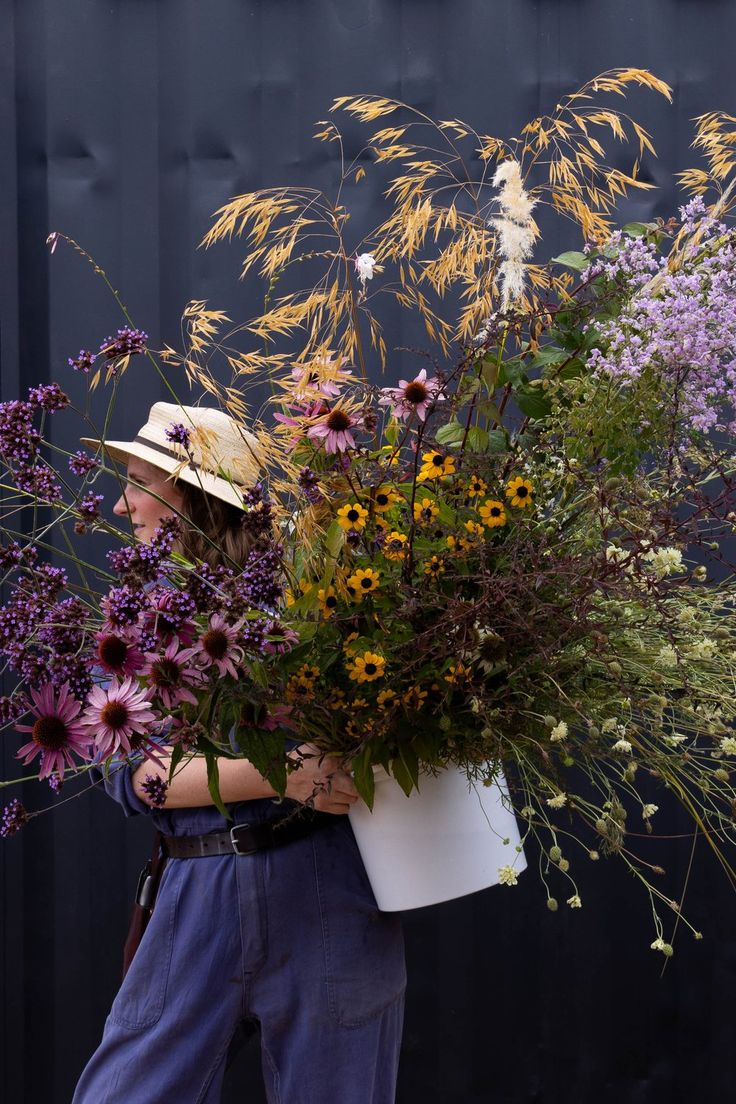 a woman carrying a large bouquet of wildflowers in front of a black wall