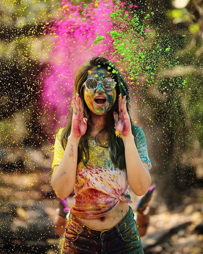 a woman covered in colored powder throwing confetti on her face and covering her eyes