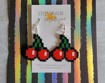 a pair of earrings with red and green beads sitting on top of a striped card