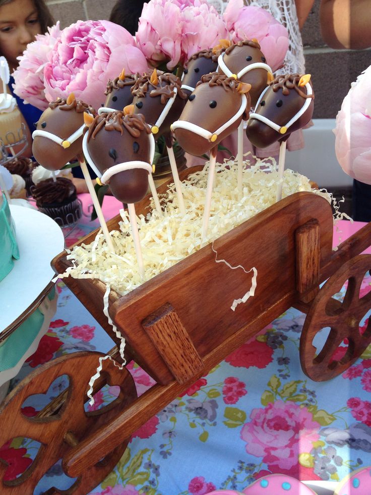 a wooden wagon filled with cake pops on top of a table next to pink flowers