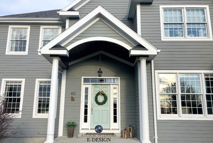 a gray house with white trim and wreath on the front door is featured in this image