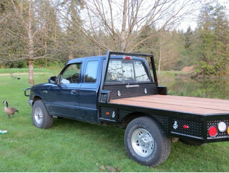 a truck with a wooden flat bed parked in the grass next to a duck pond