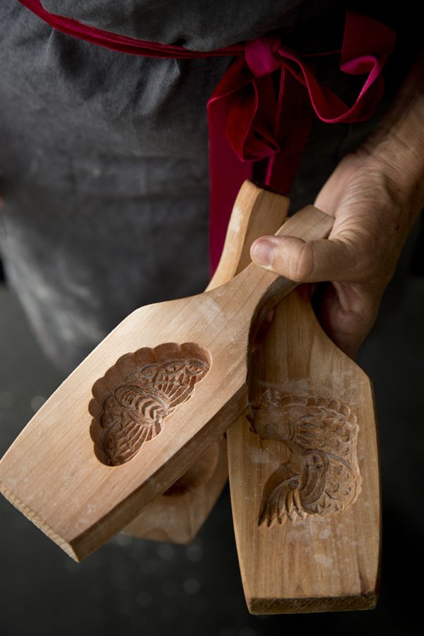 a person holding two wooden spoons with carved designs on them and one has a red ribbon around his neck