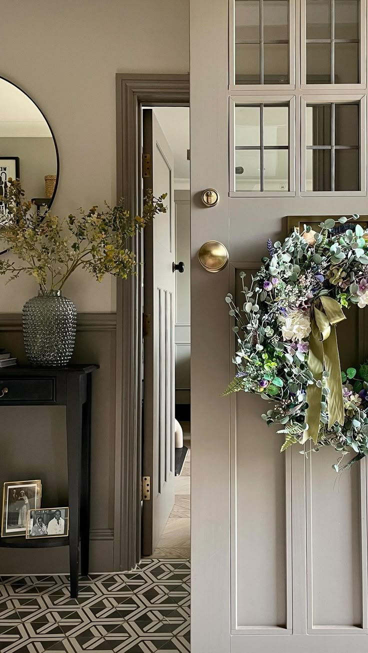 a door with a wreath on it in front of a mirror and vases filled with flowers