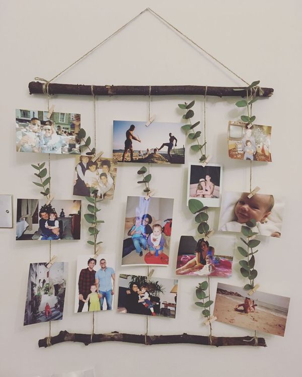 a bunch of pictures hanging on a wall next to a wooden stick with some leaves