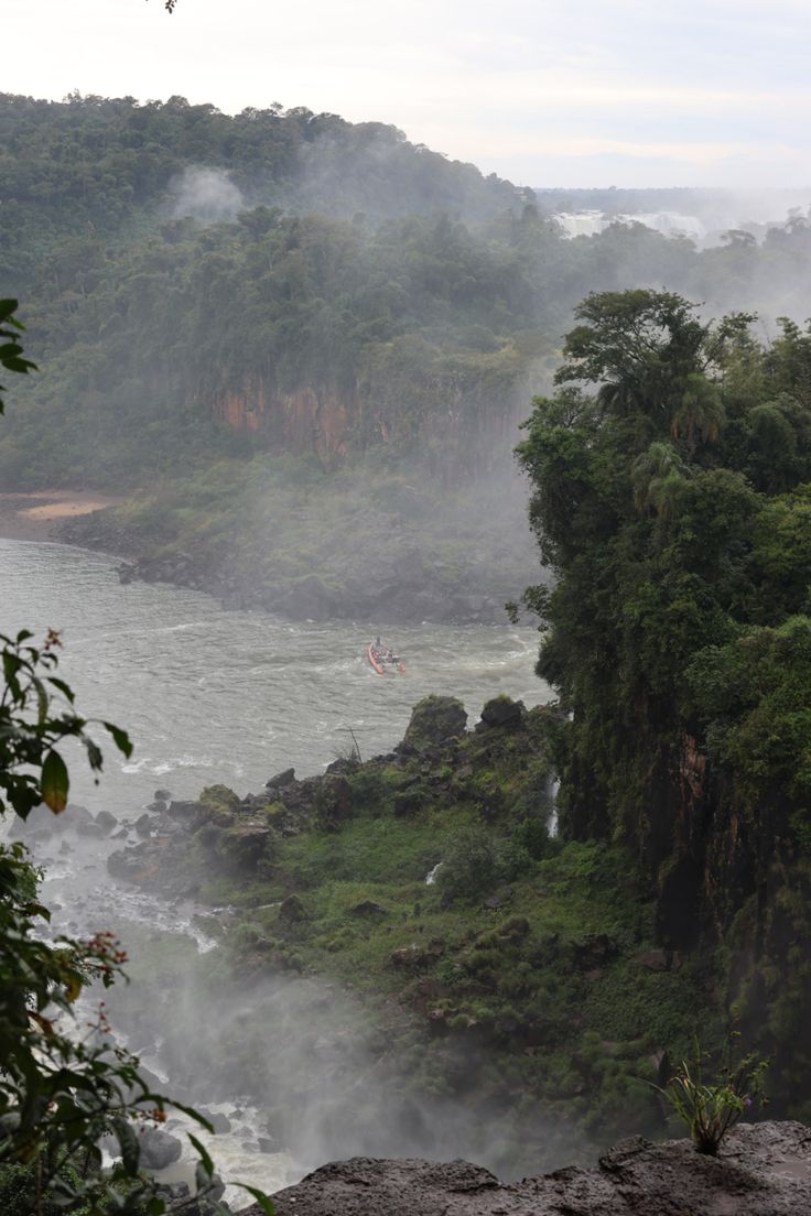 two people in canoes are on the water near some trees and mist rising from the river