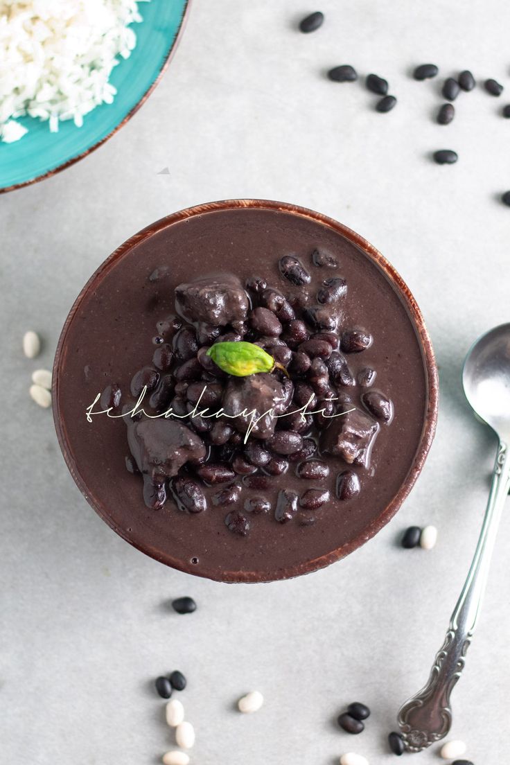 a bowl filled with chocolate pudding and beans next to a spoon on a table top