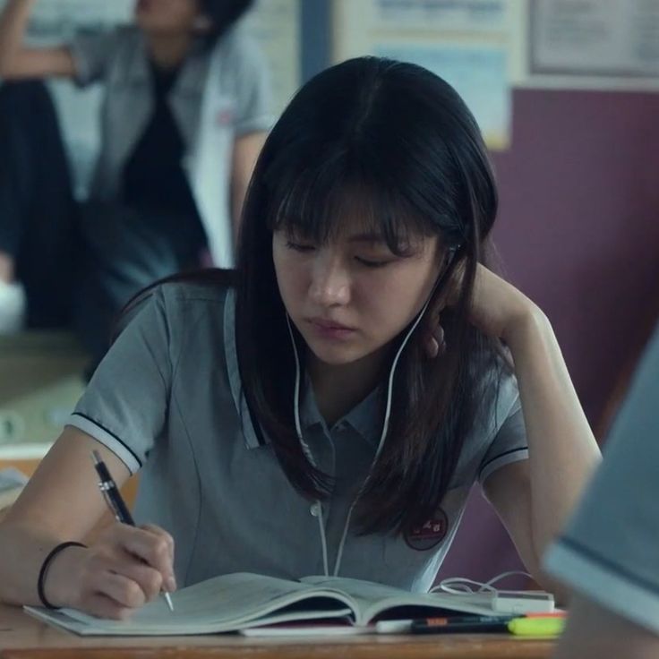 a woman sitting at a desk with headphones on writing in a book and listening to music