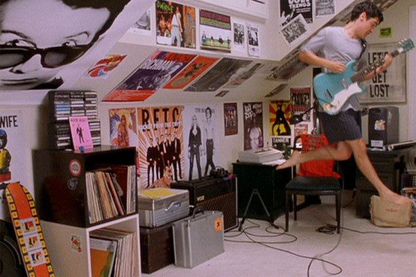 a young man playing an electric guitar in a room with posters on the walls and floor