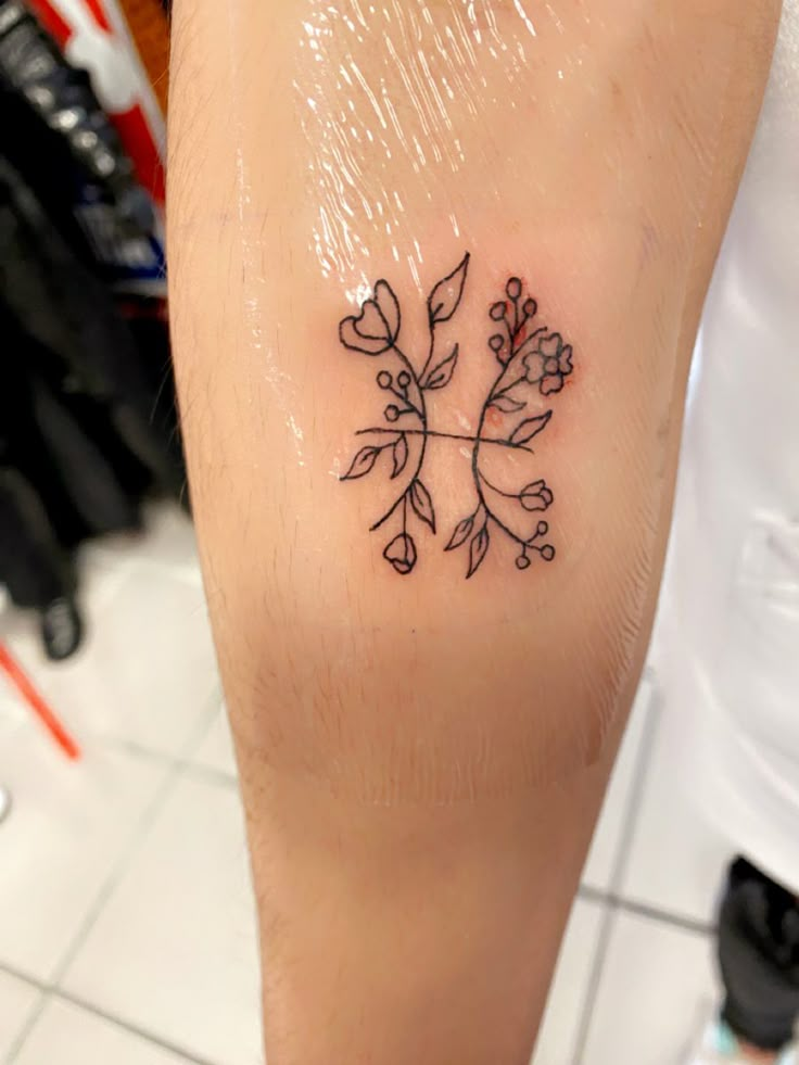 a small tattoo on the leg of a person's left arm, with flowers and leaves